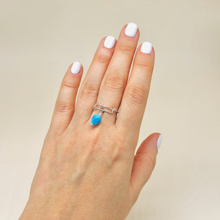 Hand wearing a silver adjustable ring with a blue stone on a beige background