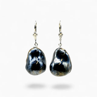 A pair of dangling earrings featuring irregular, polished dark blue baroque pearls suspended from silver leverback hooks, set against a plain white background.