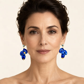 A close-up portrait of a woman wearing a pair of porcelain blue floral dangle earrings with gold accents and tiny turquoise stauds.