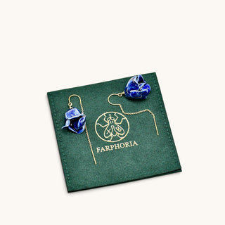 A pair of blue peony flower-shaped drop earrings with gold threaders, displayed on a dark green square pouch with the brand name FARPHORIA.