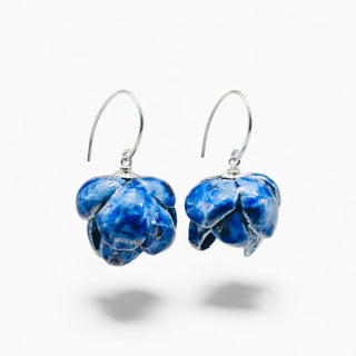 A pair of handmade blue ceramic flower-shaped dangle earrings with silver fishhook wires, shown against a plain white background.