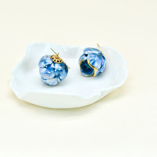 Blue glassy porcelain peony flower earrings with gold accents on a white dish