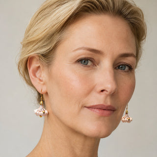 A close-up portrait of a woman with blonde hair wearing delicate gold dangle earrings with pale pink flower - perfect gift for woman who has everything.