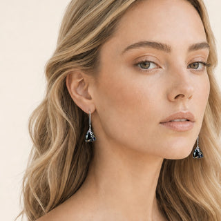 A close-up of a woman with blonde hair wearing a pair of silver drop earrings with dark flower-shaped porcelain pendants