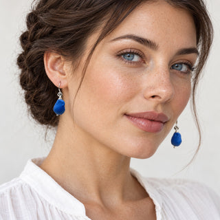 Blue-eyed model with dark braided hair wearing cobalt blue porcelain earrings and a white blouse.