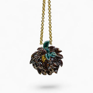 A close-up of a gold chain necklace with a textured artichoke brown pendant featuring glossy dark brown and black details, accented with small green and yellow leaf-like inlays, shown against a plain white background.