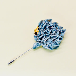 Green handmade porcelain floral brooch with golden accents on a beige background