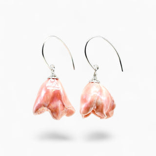 A pair of silver-tone fishhook earrings with dangling irregular pink flower charms, shown on a clean white background with soft drop shadows.