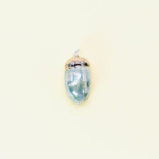 Glass acorn pendant of silver sage hue with gold top on a beige background