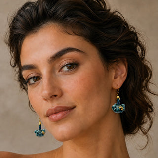 A close-up portrait of a woman wearing matching green gold floral dangle earrings - best original gift for 18th wedding anniversary.