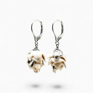 A pair of silver leverback earrings with dangling sculpted cream-colored flower charms, shown against a plain white background.