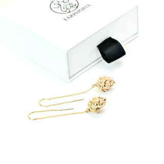 A pair of gold dangle earrings with handsculpted porcealin artichoke charms, displayed next to their white FARPHORIA branded gift packaging.