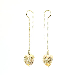 A pair of gold and cream-colored dangle earrings featuring porcelain artichokes suspended from delicate chains and hook backings, shown against a plain white background.